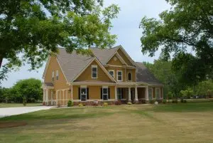 Two-story custom home by Cox Builders with a golden-yellow exterior, white trim, and a gabled roof. The design features a covered front porch, attached garage, and neatly landscaped lawn.